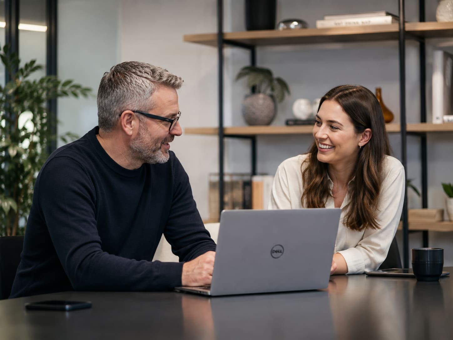 Two colleagues talking over a laptop in a bright office.
